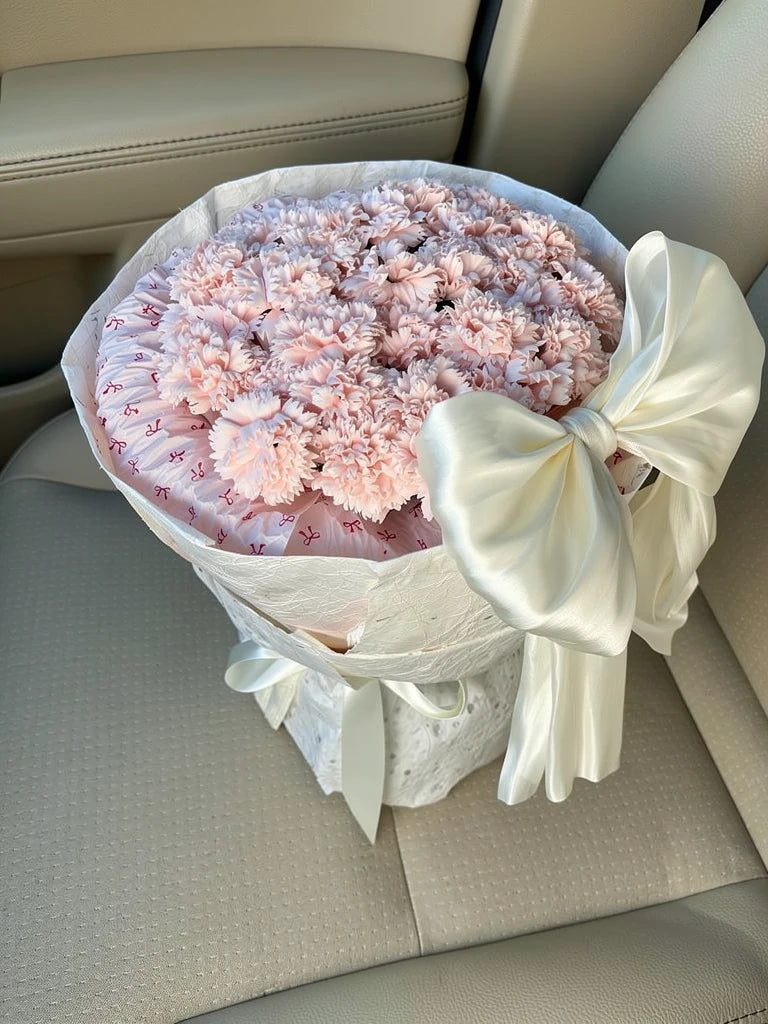 Blush Carnation Grand Bow Bouquet, Medium, high-angle car-seat view; AI lifestyle illustration
