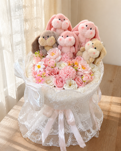 Bunny Love Bouquet with five plush bunnies, pink and ivory flowers and white lace wrapping on a sunlit table