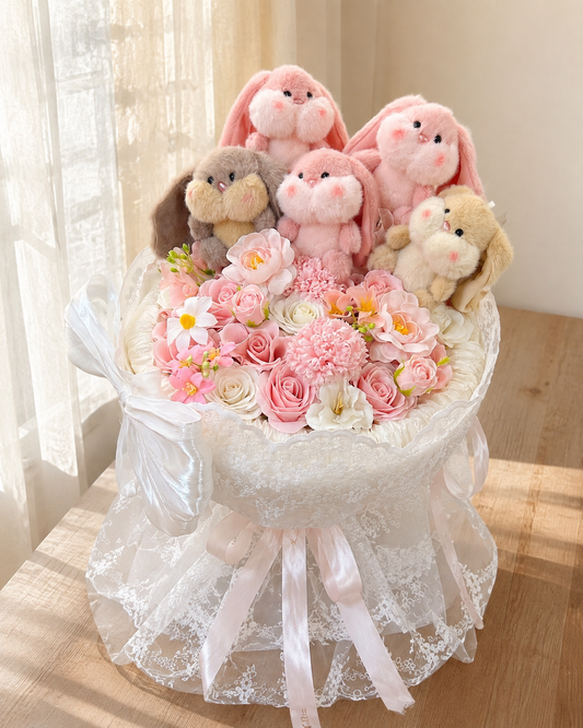 Bunny Love Bouquet with five plush bunnies, pink and ivory flowers and white lace wrapping on a sunlit table